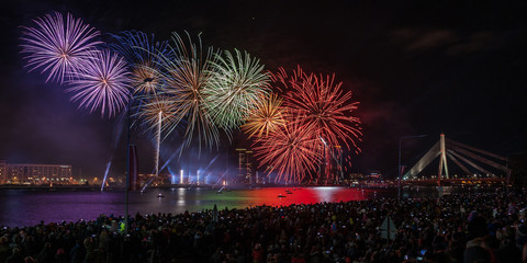 Latvian Independence Day celebrations with Saules Mūžs fireworks presentation. Riga, Latvia. Thousands of people line the River Daugava for a fireworks display timed. Panoramic view.
