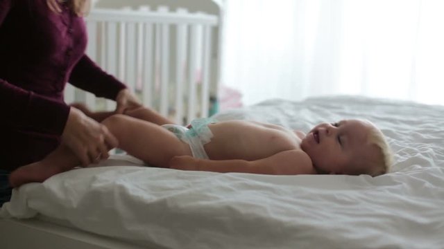 Young mom, changing baby diaper after bath in sunny bedroom