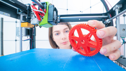 Young women designer in 3d printing lab. Girl takes the finished detail from 3D printer
