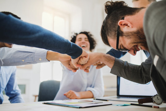 Young businesspeople sitting around table in a modern office, making fist bump.