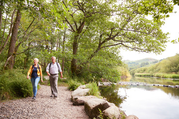 Senior Couple Hiking Along Path By River In UK Lake District