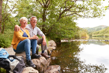 Fototapeta premium Senior Couple On Hike Sitting By River In UK Lake District