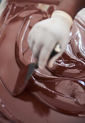 Confectionary factory worker mixing melted chocolate with a spatula 
