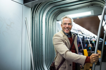 Mature businessman with smartphone travelling by tram in city.