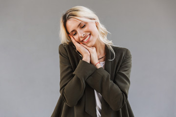 Image of pleased woman 20s wearing jacket smiling and touching face, isolated over gray background