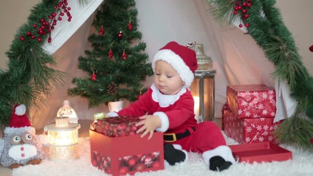 Adorable little toddler baby boy dressed in canta claus costume, playing at home in front of teepee decorated for Christmas