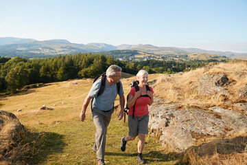 Senior Couple Climbing Hill On Hike Through Countryside In Lake District UK Together