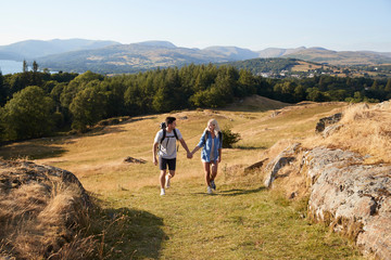 Couple Climbing Hill On Hike Through Countryside In Lake District UK Together