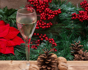 Winter holiday decoration: Blooming Red Poinsettia, Pine and Berry bush, cone, walnut  and glass of white wine on wooden background.