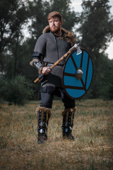 Warrior Viking in full arms with axe and shield in dark forest waiting for battle