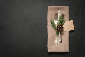Christmas table place setting with silverware and dark natural evergreen decor. Holiday background.