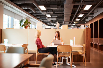 Two Young Businesswomen Having Informal Interview In Cafeteria Area At Graduate Recruitment Assessment Day