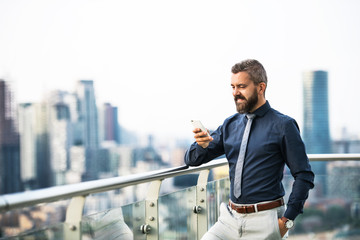 A portrait of businessman with smartphone standing against London view panorama.