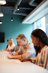 Group Of Young Candidates Sitting At Boardroom Table Making Notes At Presentation At Business...