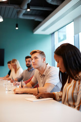 Group Of Young Candidates Sitting At Boardroom Table Making Notes At Presentation At Business Graduate Recruitment Assessment Day