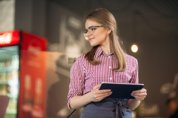 Attractive young waitress using a tablet computer to take an order from a customer in a coffee shop