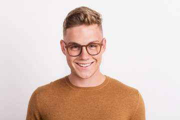 A confident young man in a studio, wearing glasses.