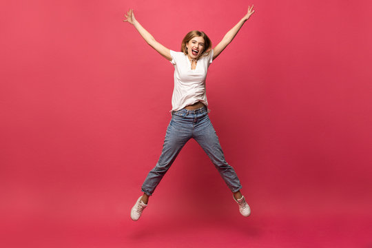 happiness, freedom, motion and people concept - smiling young woman jumping in air over pink background