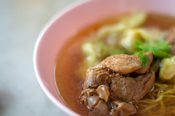 The yellow egg noodle and wonton with duck drum stick and green coriander and brown hot soup in the pink bowl.