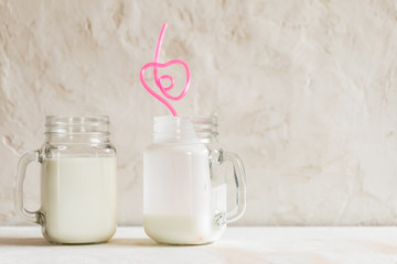Two glass jars with kefir and pink drinking tube in heart form are standing on white background...