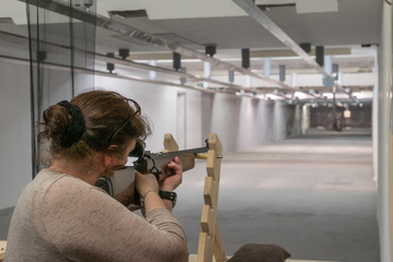 Frau mit Dutt zielt auf auf einer Schießanlage mit einem Gewehr 