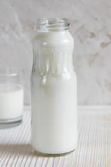 Close-up bottle with kefir is standing on white wooden table on white background.