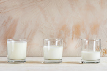 Three glasses with kefir are standing in row on white table on light background.