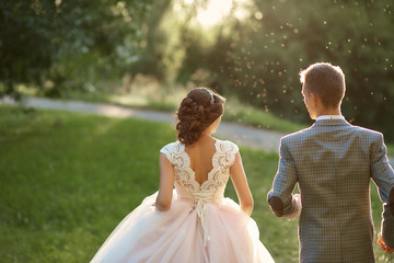 Just married loving hipster couple in wedding dress and suit on green field in a forest at sunset....