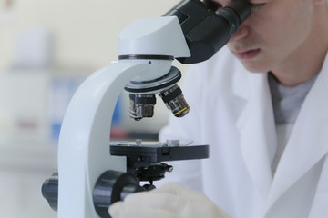 Young male scientist looking through a microscope in a laboratory doing research, microbiological analysis, medicine.