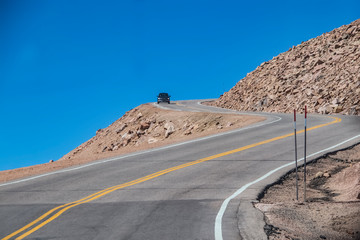 Car rounding sharp bend with steep dropoff on dangerous mountain road with blue sky behind