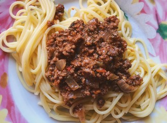 Top view on a plate with spaghetti topped with fried force meat in vegetable sauce 