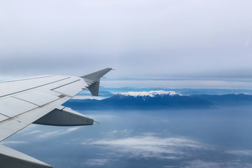 Fototapeta premium View from airplane with wing flying over Mt Olympus Greece with the snow-covered peak showing through a heavy fog