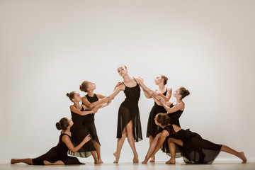 The group of modern ballet dancers dancing on gray studio background