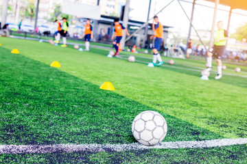 Ball on green artificial turf at side line of football field with blurry players are training...