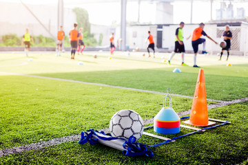 Football and soccer training equipment on green artificial turf with blurry players training background.