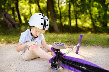 Toddler boy in safety helmet learning to ride scooter