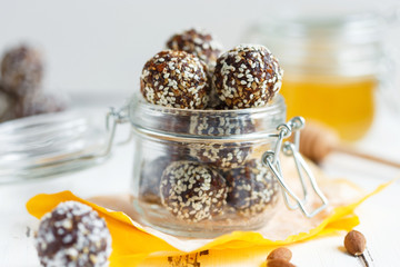 healthy energy granola bites with nuts, dates, honey and sesame in a glass jar on a white table