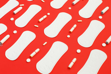 Pile of white pads many tampons and pills on red background.