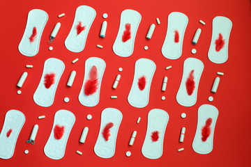 Red feather and pile of white pads many tampons and pills on red background. Menstruation, hygiene protection means.