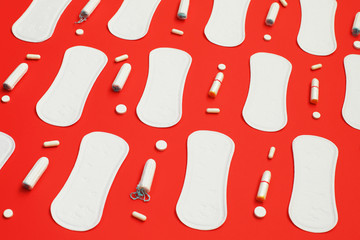 Pile of white pads many tampons and pills on red background.