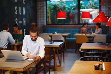 Young man taking notes from a laptop in cafe