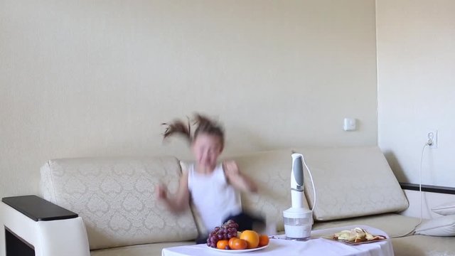 Child jumps on the couch with joy. Girl jumping gallos having fun alone in the room.