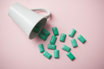 closeup of peppermint chewing gum falling from a white cup on pink background