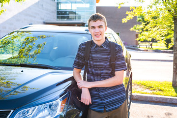 Happy male teenager leaning against his car in a high school parking lot.