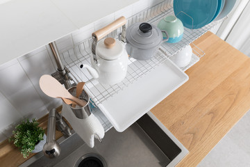 Clean dishes drying on metal dish rack on light background. Kitchen utensils and dishware on wooden shelf. Kitchen interior background.Text space.