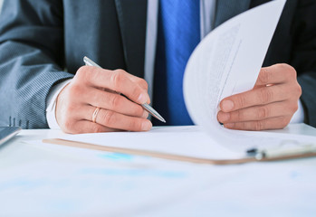 Businessman in dark suit sitting at office desk signing a contract with shallow focus on signature.