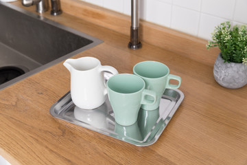 Clean dishes drying on metal dish rack on light background. Kitchen utensils and dishware on wooden shelf. Kitchen interior background.Text space.