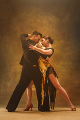 The young dance ballroom couple in gold dress dancing in sensual pose on studio background....