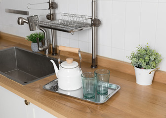 Clean dishes drying on metal dish rack on light background. Kitchen utensils and dishware on wooden shelf. Kitchen interior background.Text space.