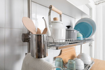 Clean dishes drying on metal dish rack on light background. Kitchen utensils and dishware on wooden...